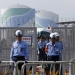 Police officers and security personnel stand guard at an entrance of Kyushu Electric Power's Sendai nuclear power station, during a protest demanding for the stop of the plant's restart, in Satsumasendai, Kagoshima prefecture, Japan August 9, 2015. Japan switched on a nuclear reactor for the first time in nearly two years on Tuesday, as Prime Minister Shinzo Abe seeks to reassure a nervous public that tougher standards mean the sector is now safe after the Fukushima disaster in 2011. The No.1 (L) and No.2 reactor buildings are seen in the background. Picture taken August 9, 2015. REUTERS/Issei Kato - RTX1NTTZ