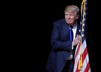 Donald Trump hugs a U.S. flag as he takes the stage for a campaign town hall meeting in Derry, New Hampshire August 19, 2015. REUTERS/Brian Snyder