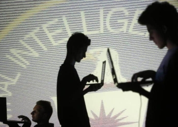 People are silhouetted as they pose with laptops in front of a screen projected with binary code and a Central Inteligence Agency (CIA) emblem, in this picture illustration taken in Zenica October 29, 2014. REUTERS/Dado Ruvic