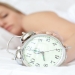 Blond woman holding an alarm clock and sleeping on her bed