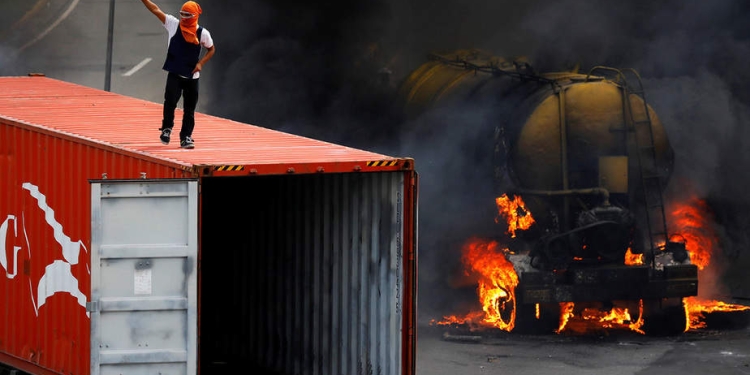 Un manifestante se alza sobre un camión incendiado para construir una barricada mientras manifiesta en contra el gobierno del presidente de Venezuela, Nicolás Maduro, en Caracas, Venezuela.