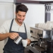 Portrait of a young waiter smiling and making cup of coffee at coffee shop