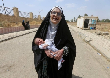 Una anciana iraquí desplazada que huyó de militantes islámicos lleva a un bebé en Mosul, Irak