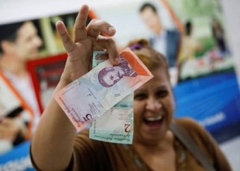 Una mujer sonríe mientras muestra los nuevos dos y cinco billetes de Bolívar Soberano, después de que los retiró de un cajero automático  en una sucursal del banco Mercantil en Caracas