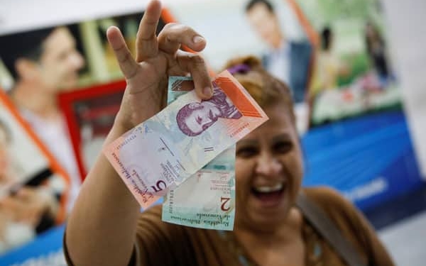 Una mujer sonríe mientras muestra los nuevos dos y cinco billetes de Bolívar Soberano, después de que los retiró de un cajero automático  en una sucursal del banco Mercantil en Caracas