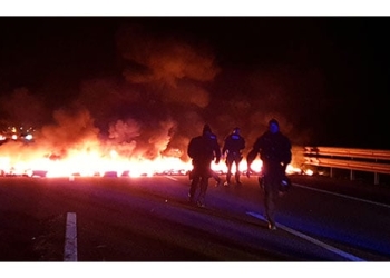 Agentes de policía junto a barricadas en llamas que intentaron bloquear la autopista AP7 durante una huelga general cerca de Girona.