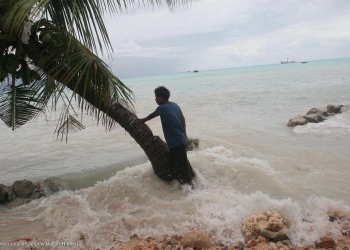 Residente local se apoya contra una palmera mientras las altas olas causadas por las 'Mareas del Rey' entran en la propiedad de su familia, Betio Villge, Isla Tarawa, Kiribati, Océano Pacífico.