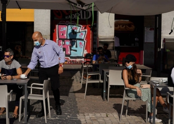 Un camarero que usa una máscara facial protectora sirve una bebida para un cliente en una sección de un restaurante al aire libre que reabrió por primera vez en más de 2 meses en medio del brote de la enfermedad por coronavirus (COVID-19), en la Plaza Mayor de Madrid, España, 25 de mayo de 2020. REUTERS / Juan Medina