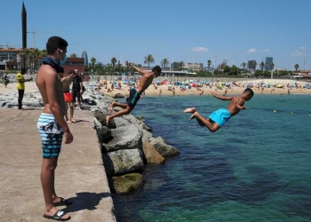 Hombres se lanzan al agua mientras que disfrutan del sol en la playa después de que se anunciaron limitaciones para contener la propagación de la enfermedad por el nuevo coronavirus COVID-19 en Barcelona, España. 19 de julio de 2020. REUTERS/Nacho Doce